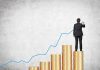 Businessman standing on stacks of coins, drawing a growth chart