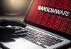 Gloved hand on laptop with ransomware screen.