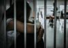 Person sitting behind bars with arms wrapped around knees