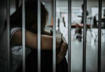 Person sitting behind bars with arms wrapped around knees