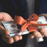 Hands holding stack of hundred-dollar bills with ribbon