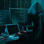 Hacker in dark room surrounded by computer screens