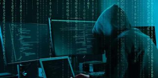 Hacker in dark room surrounded by computer screens