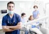 A dentist smiling in a dental office with a team assisting a patient