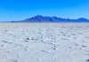 A vast salt flat with a mountain range in the background under a clear blue sky