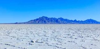 A vast salt flat with a mountain range in the background under a clear blue sky