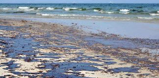 Oil spill on a sandy beach with waves in the background