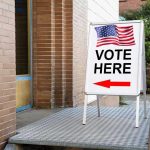 Vote Here sign with arrow and American flag