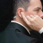 Man in suit adjusts earpiece with finger