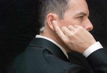 Man in suit adjusts earpiece with finger