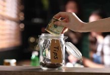 Hand placing dollar bill into a tip jar