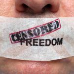 Close up of a persons mouth covered with tape that reads CENSORED FREEDOM
