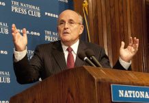 A man in a suit speaking at a podium during a press conference